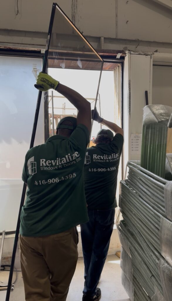 two revitalize windows and doors employees lifting and carrying a storefront replacement glass unit.