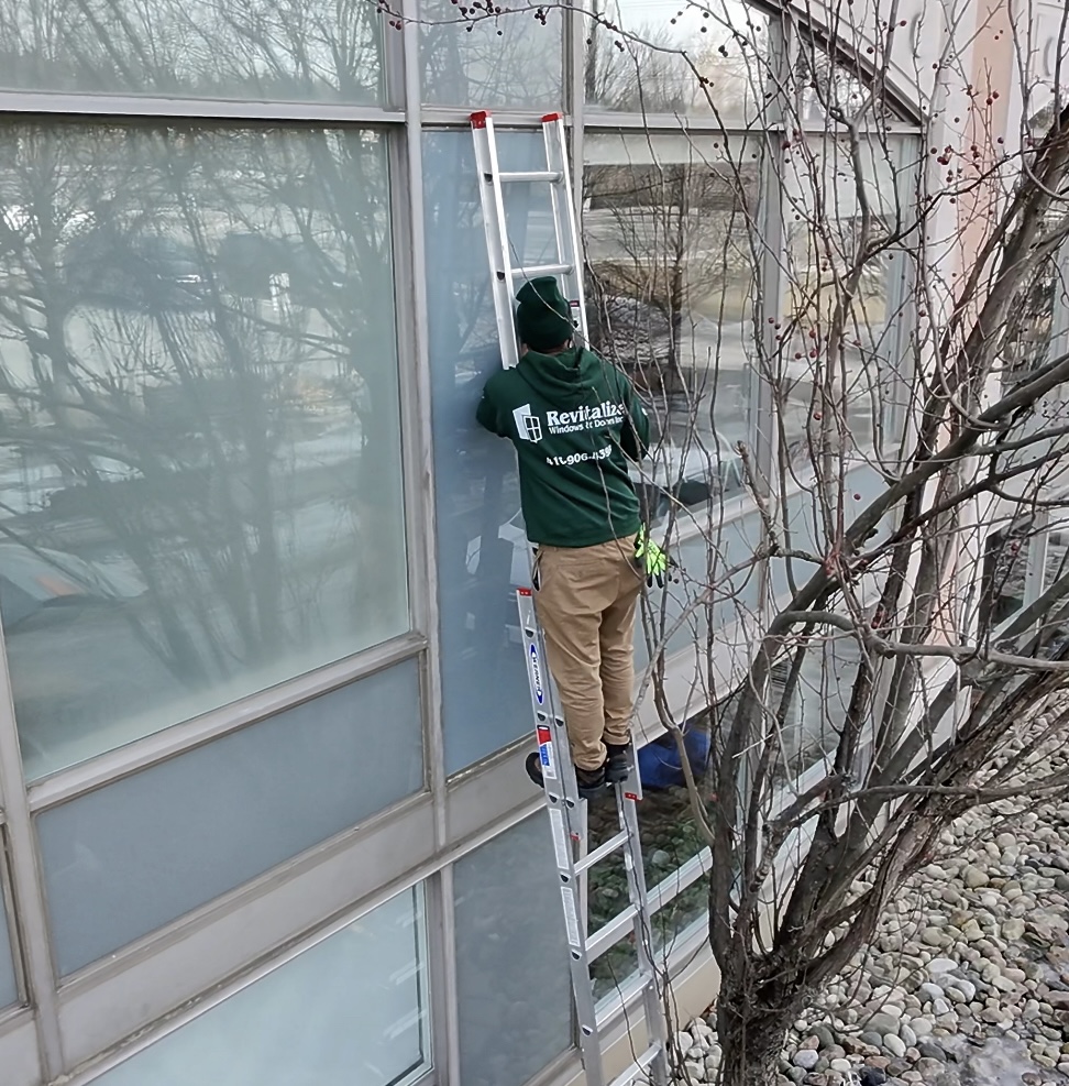 revitalize windows and doors technician on ladder repairing window.